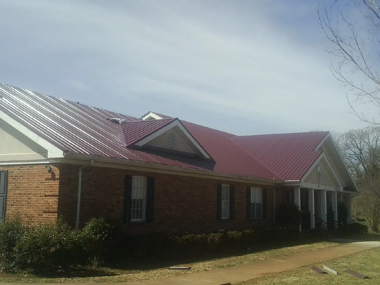 Red metal roof with gabled entries on a long brick building, from a Hail Damage Roof Repair job in Bear Creek