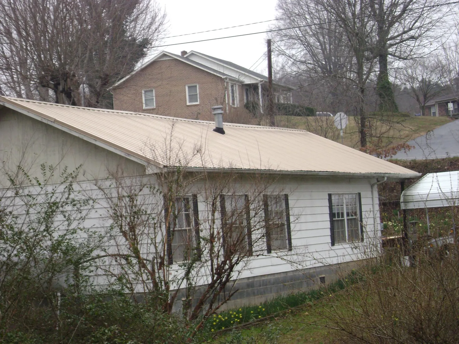 Tan metal roof on a white sided house set into a hillside — Commercial Roofing by Roofing Brothers in Bear Creek